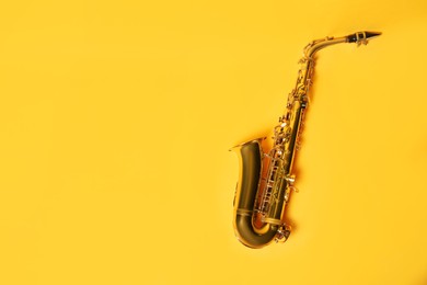 Photo of Beautiful saxophone on yellow background, top view. Space for text