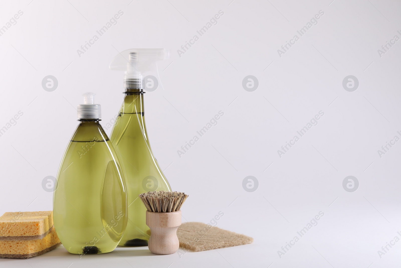 Photo of Bottles of cleaning product, brush and sponges on white background