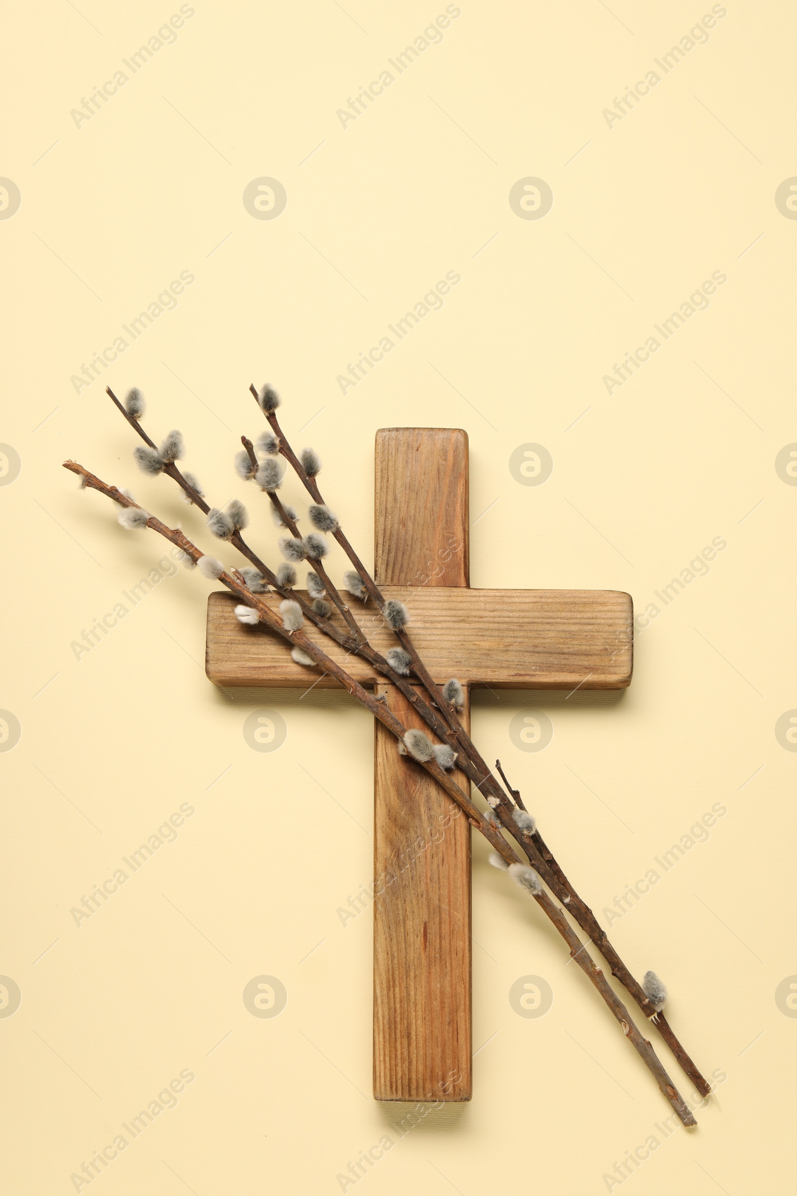 Photo of Wooden cross and willow branches on beige background, top view. Easter attributes