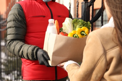 Photo of Courier giving paper bag with groceries to woman outdoors, closeup. Delivery service during Covid-19 quarantine