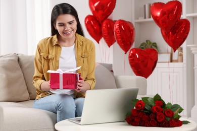 Photo of Valentine's day celebration in long distance relationship. Woman holding gift box while having video chat with her boyfriend via laptop at home