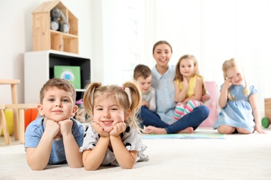 Photo of Playful little children lying on floor indoors. Space for text