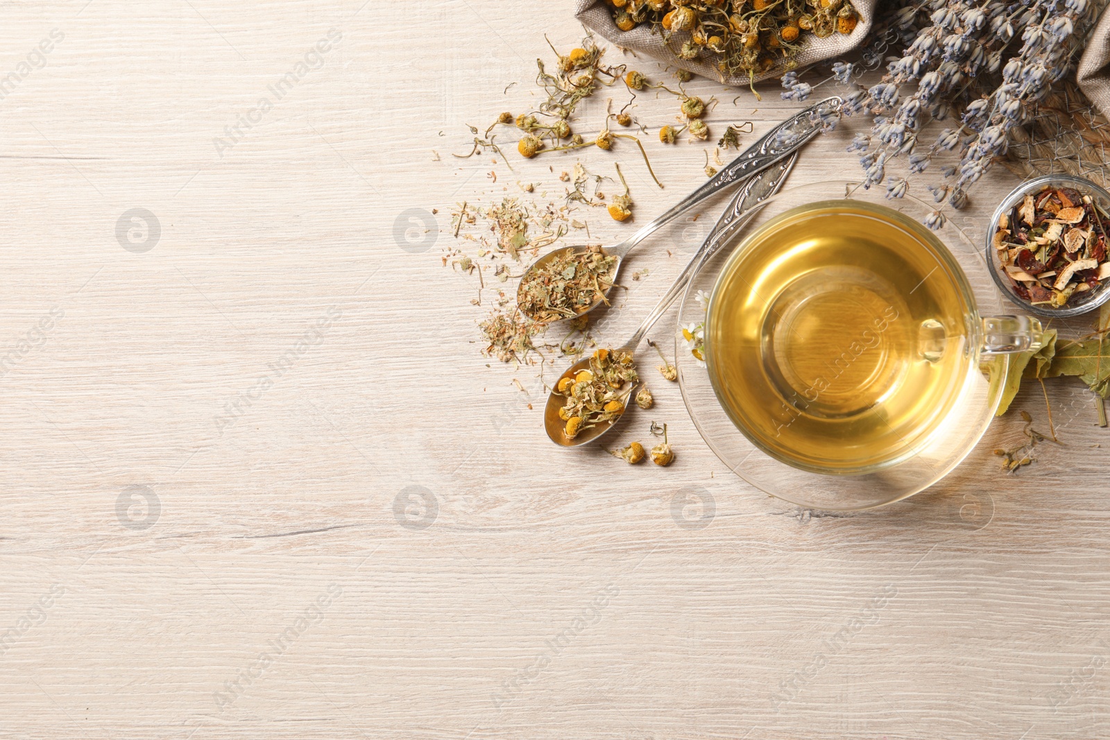 Photo of Glass cup of aromatic freshly brewed tea near different dry herbs on wooden table, flat lay. Space for text