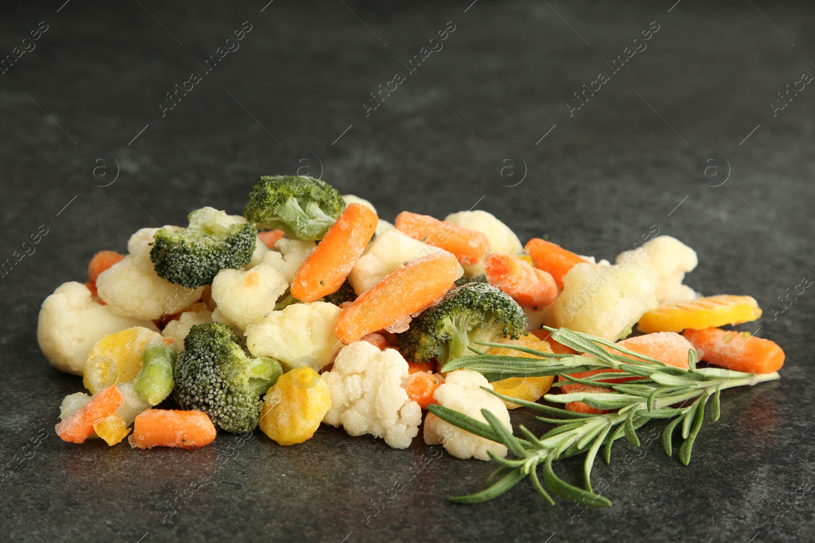 Photo of Mix of different frozen vegetables and rosemary on gray table, closeup