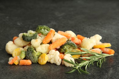 Photo of Mix of different frozen vegetables and rosemary on gray table, closeup