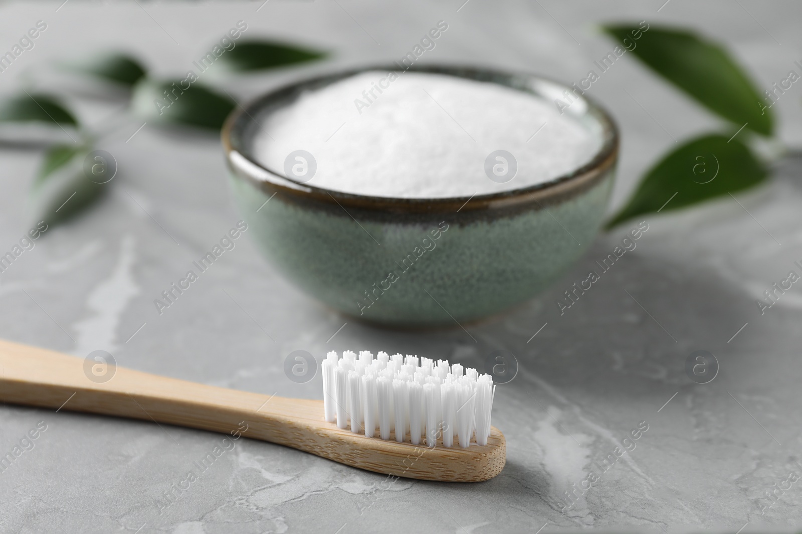 Photo of Bamboo toothbrush and bowl of baking soda on light gray marble table, closeup