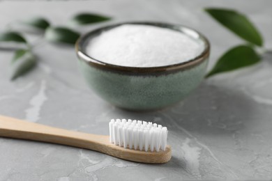 Bamboo toothbrush and bowl of baking soda on light gray marble table, closeup