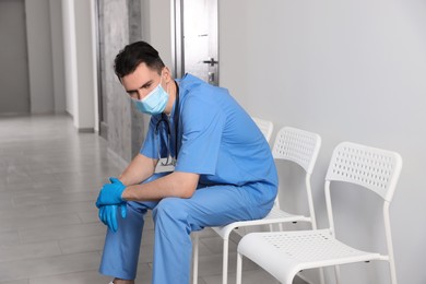 Exhausted doctor sitting on chair in hospital hallway