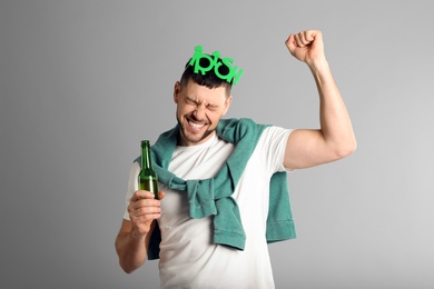 Emotional man in St Patrick's Day outfit with beer on light grey background