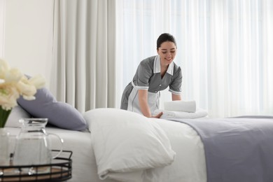 Photo of Young maid putting stack of towels onto bed in hotel room
