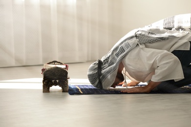 Photo of Muslim man in traditional clothes praying on rug indoors