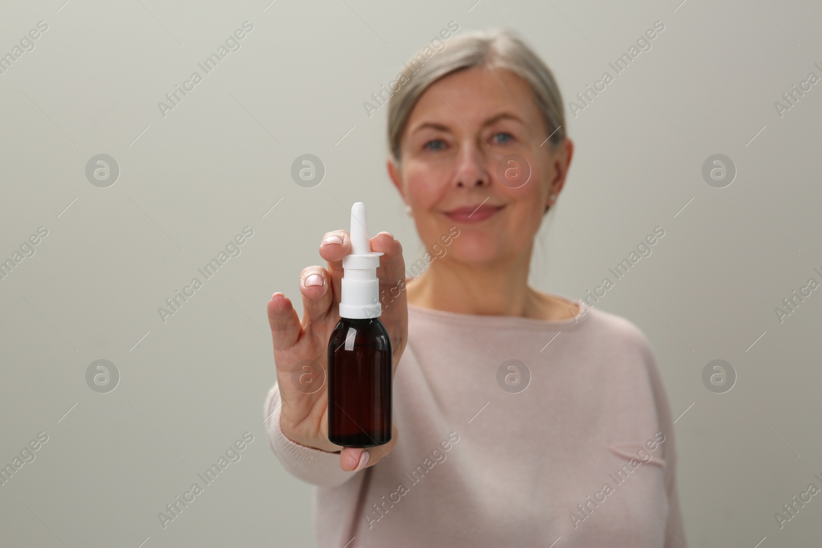 Photo of Woman holding nasal spray against light grey background, focus on bottle