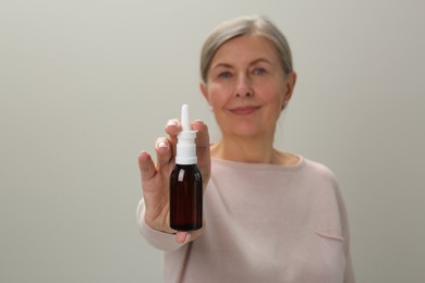 Woman holding nasal spray against light grey background, focus on bottle