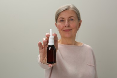 Photo of Woman holding nasal spray against light grey background, focus on bottle