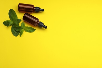 Photo of Bottles of essential oil and mint on yellow background, flat lay. Space for text