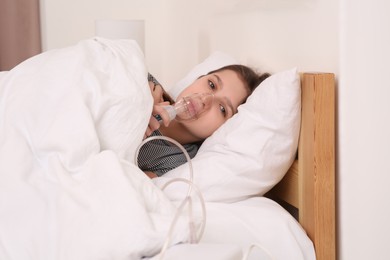 Photo of Cute girl using nebulizer for inhalation on bed at home