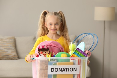 Photo of Cute little girl holding donation box with toys at home