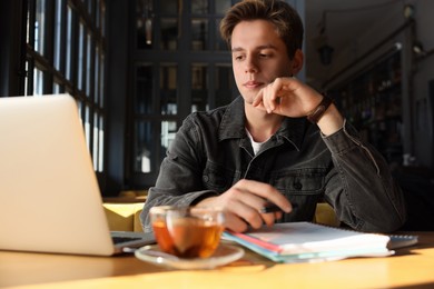 Teenage student with laptop studying at table in cafe