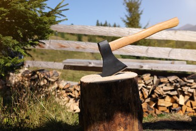 Photo of Tree stump with axe and cut firewood outdoors, space for text