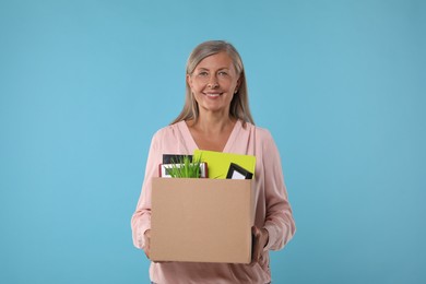 Photo of Happy unemployed senior woman with box of personal office belongings on light blue background