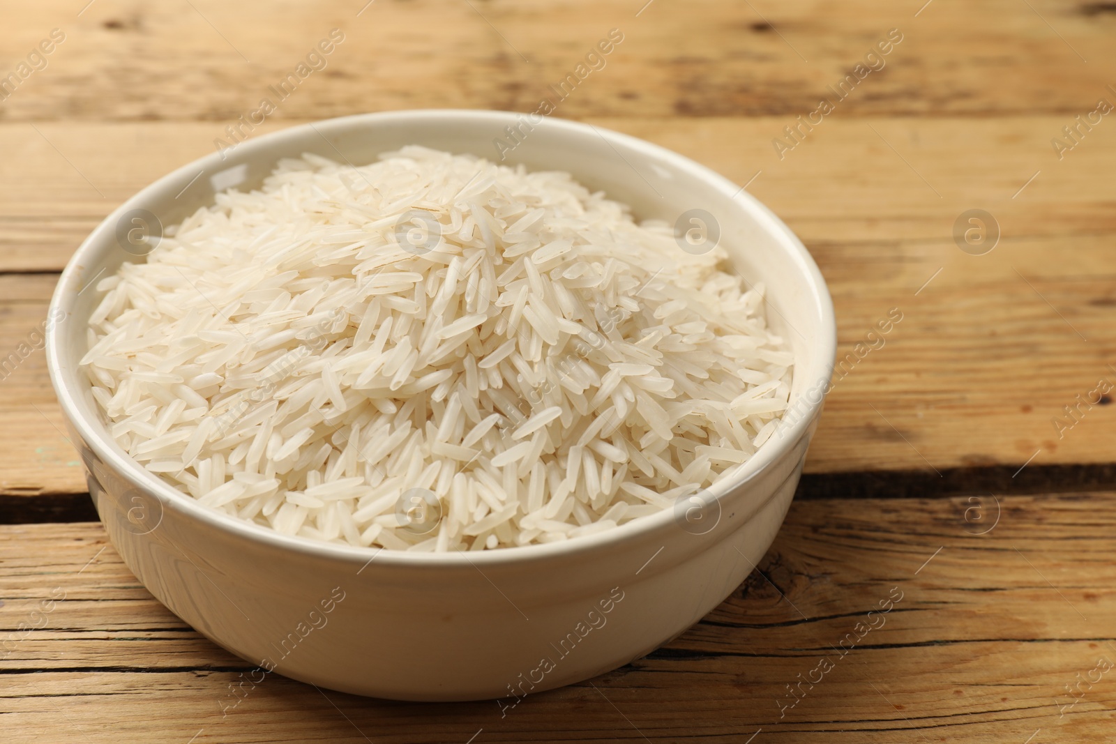 Photo of Raw basmati rice in bowl on wooden table