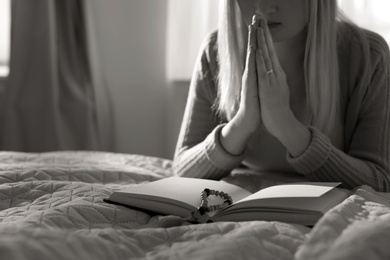 Photo of Religious young woman praying over Bible in bedroom. Black and white effect