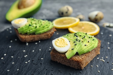 Rye toast with sliced avocado and quail eggs on slate plate, closeup