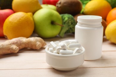 Photo of Dietary supplements. Bottle and bowl with pills near food products on light wooden table, closeup