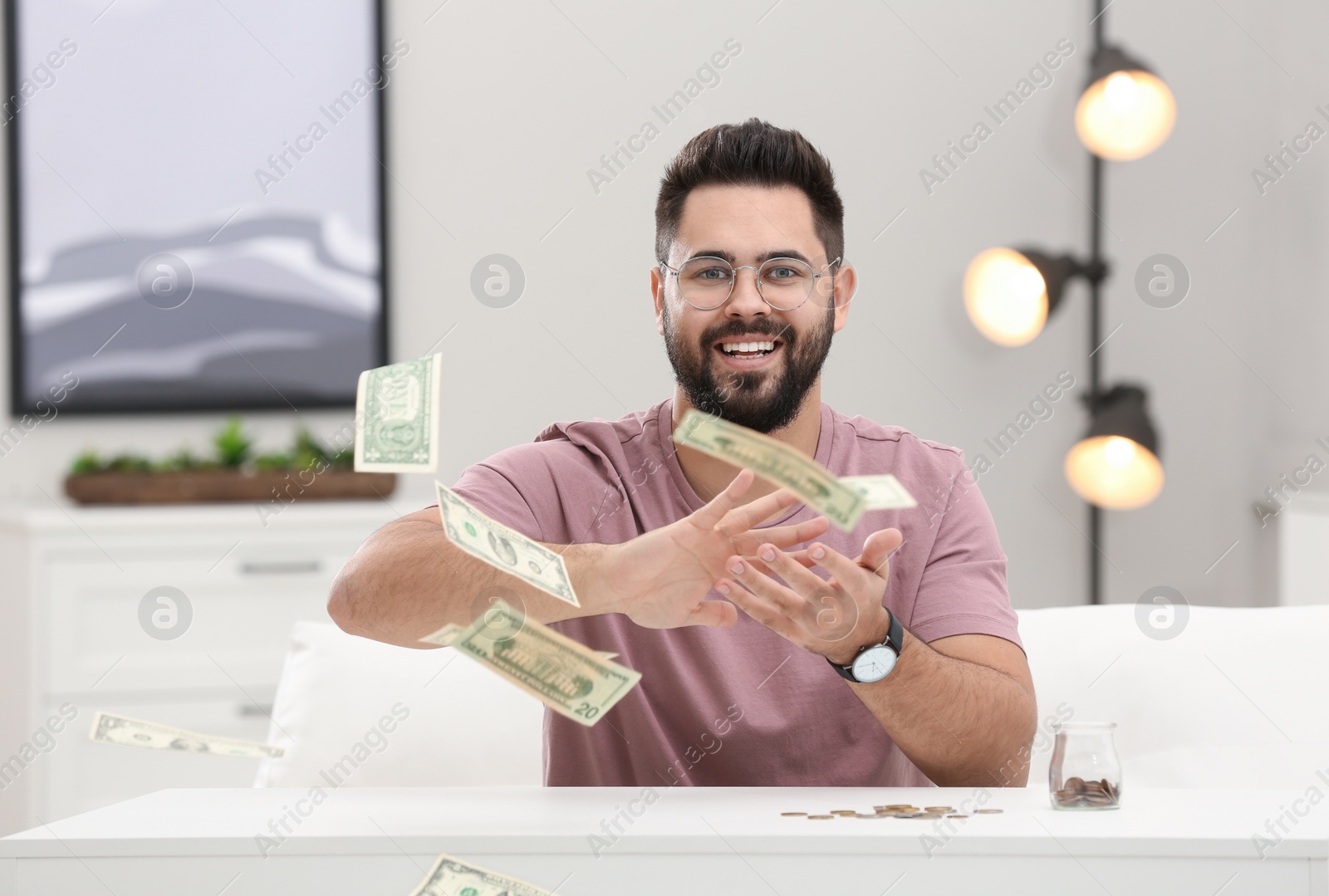 Photo of Happy young man throwing money at white table indoors