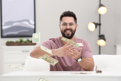 Photo of Happy young man throwing money at white table indoors