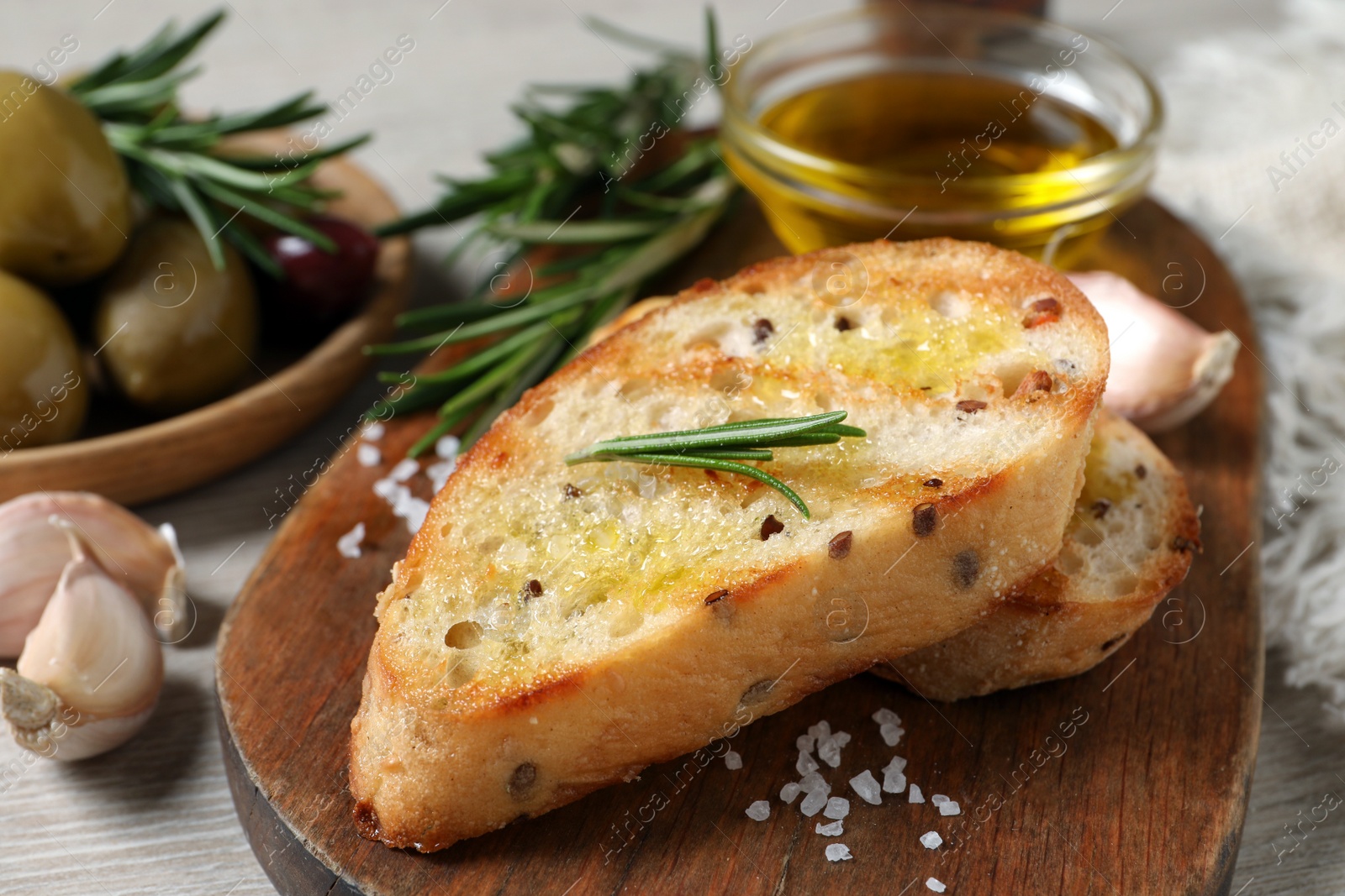 Photo of Tasty bruschettas with oil and rosemary on wooden board, closeup