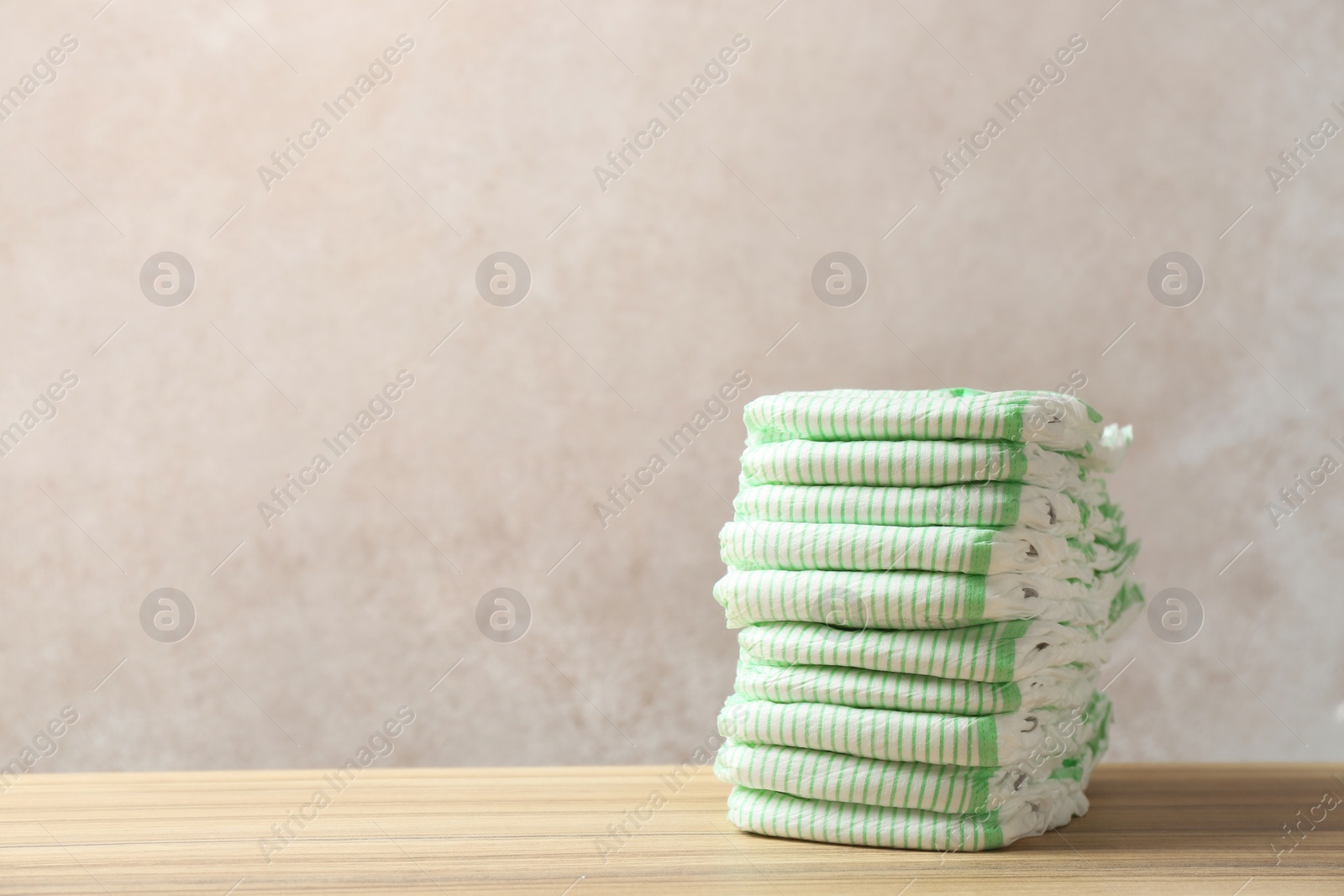Photo of Stack of diapers on table against color background, space for text. Baby accessories