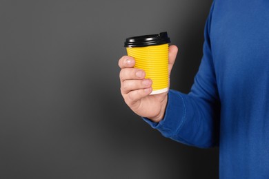 Photo of Man holding takeaway cup with drink on dark grey background, closeup view and space for text. Coffee to go