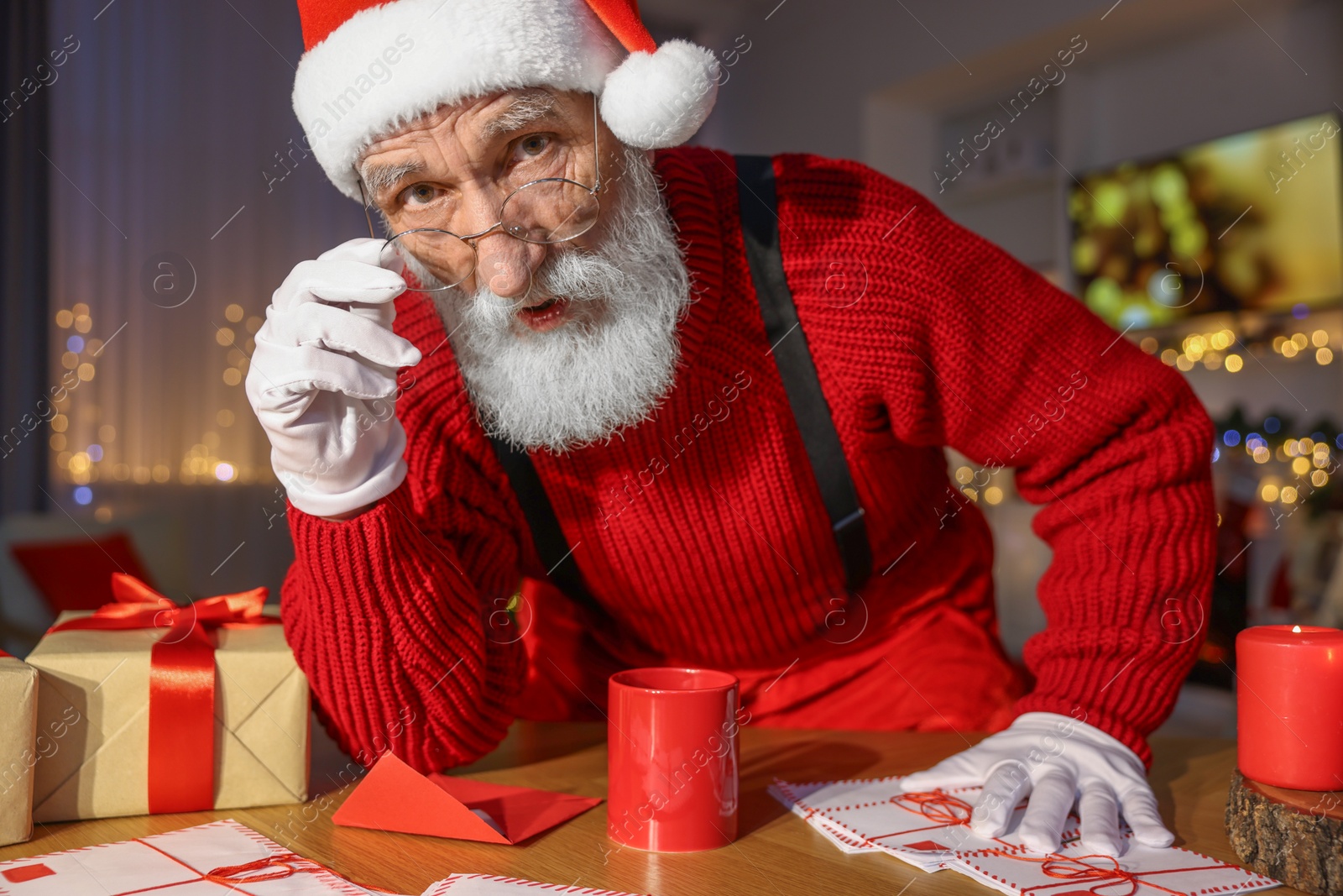 Photo of Santa Claus looking into camera at his workplace in room decorated for Christmas