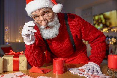 Santa Claus looking into camera at his workplace in room decorated for Christmas