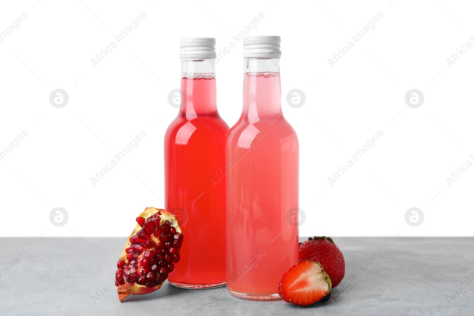Photo of Delicious kombucha in glass bottles, pomegranate and strawberry on grey table against white background