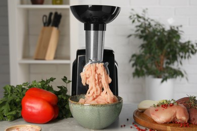 Photo of Electric meat grinder with chicken mince and products on grey marble table indoors