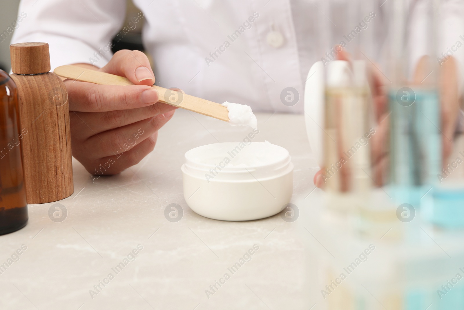 Photo of Dermatologist developing cosmetic product at light marble table, closeup