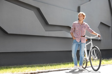 Photo of Handsome young man with bicycle near gray wall outdoors. Space for text