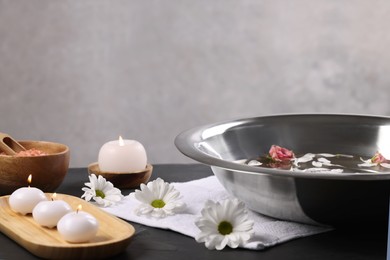 Photo of Bowl of water, flowers, burning candles and sea salt on dark table. Pedicure procedure