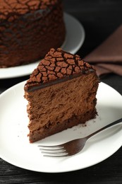 Photo of Piece of delicious chocolate truffle cake and fork on black wooden table, closeup