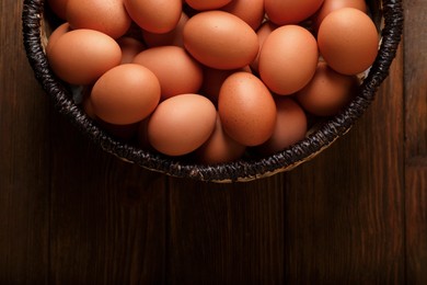 Photo of Raw chicken eggs in wicker basket on wooden table, top view. Space for text