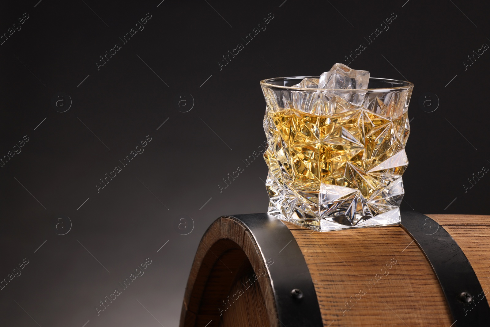 Photo of Whiskey in glass on wooden barrel against dark background, space for text