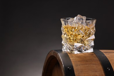 Photo of Whiskey in glass on wooden barrel against dark background, space for text