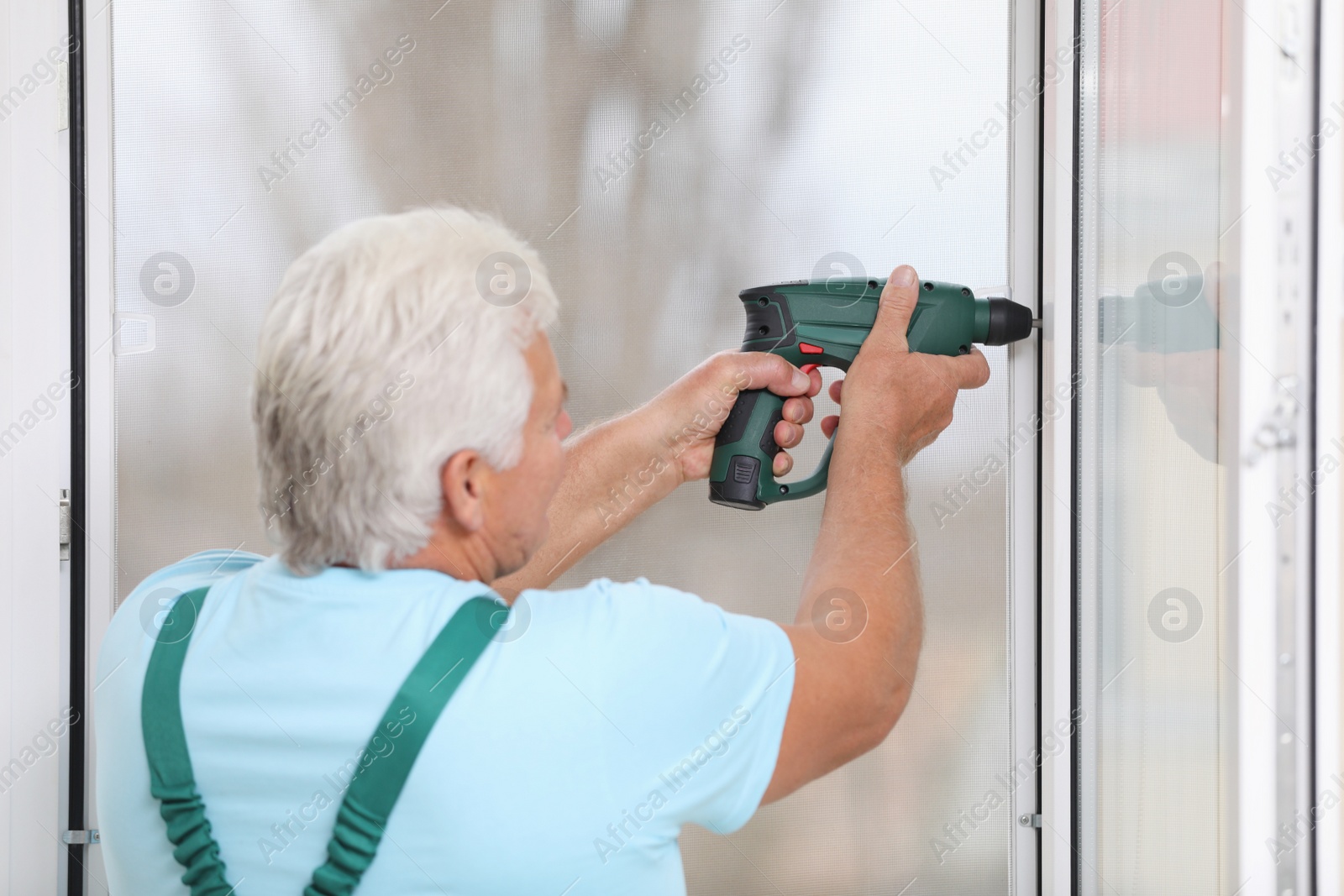 Photo of Mature construction worker repairing plastic window with electric screwdriver indoors