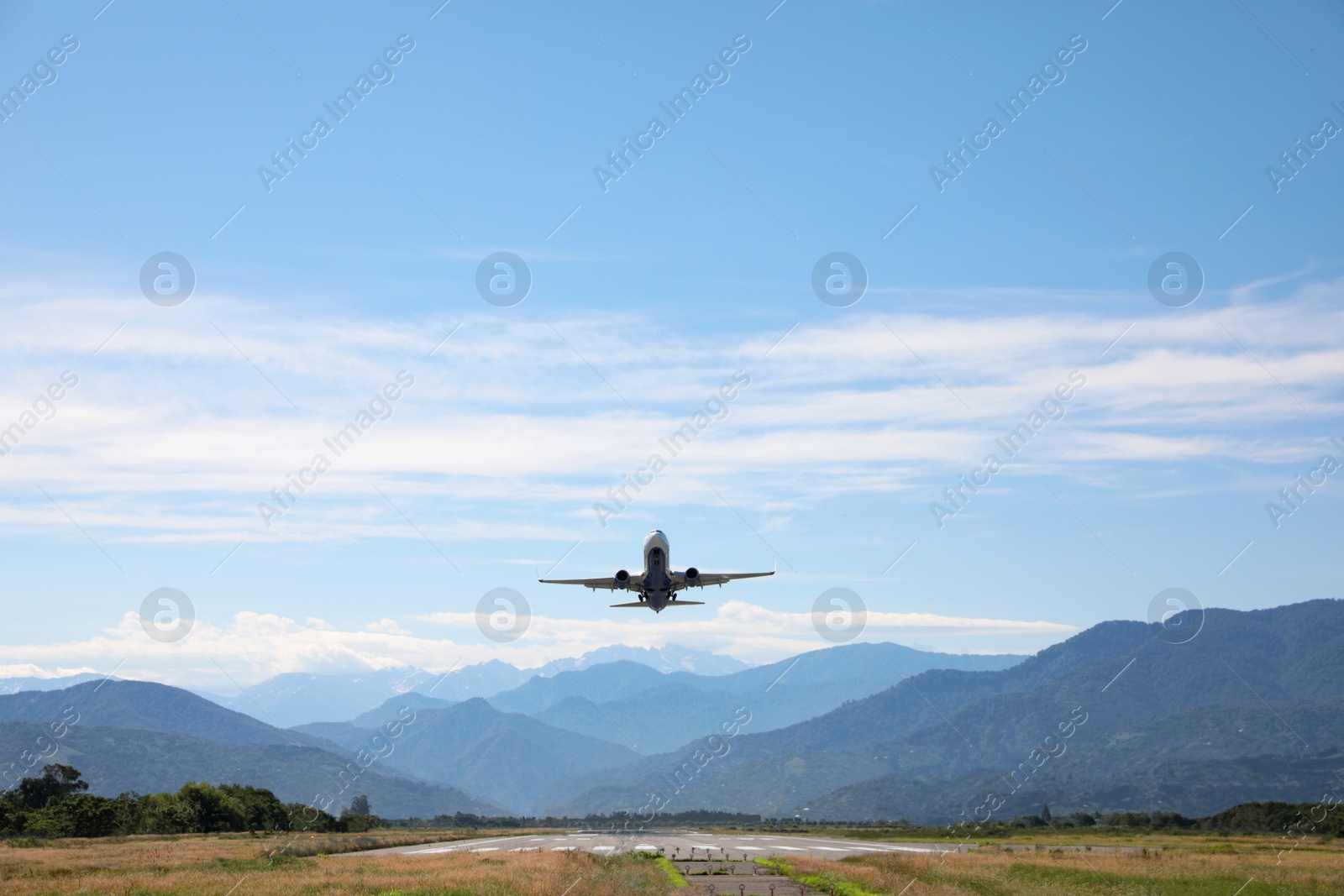 Photo of Modern white airplane landing on runway near mountains