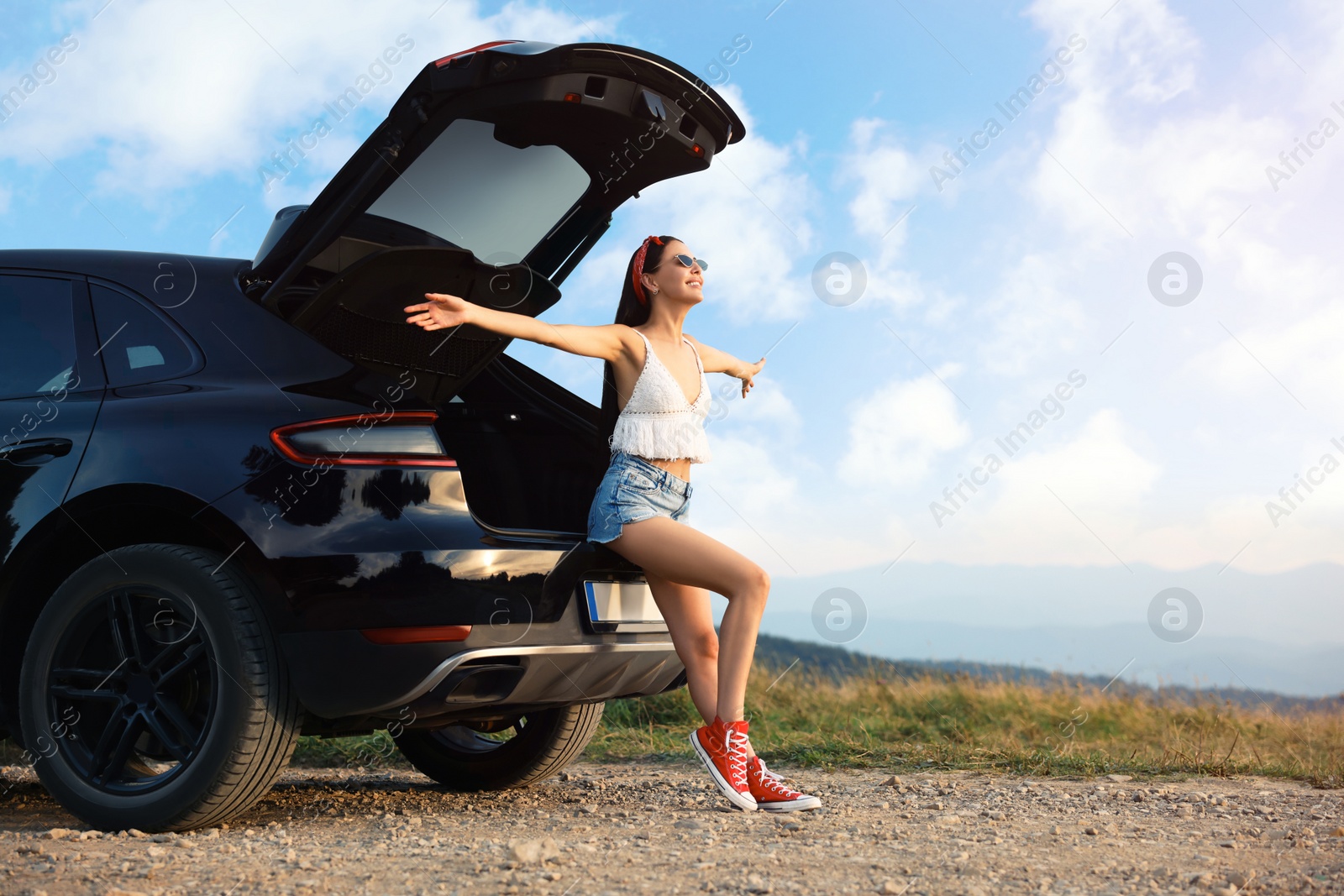 Photo of Happy woman sitting in trunk of modern car on roadside outdoors