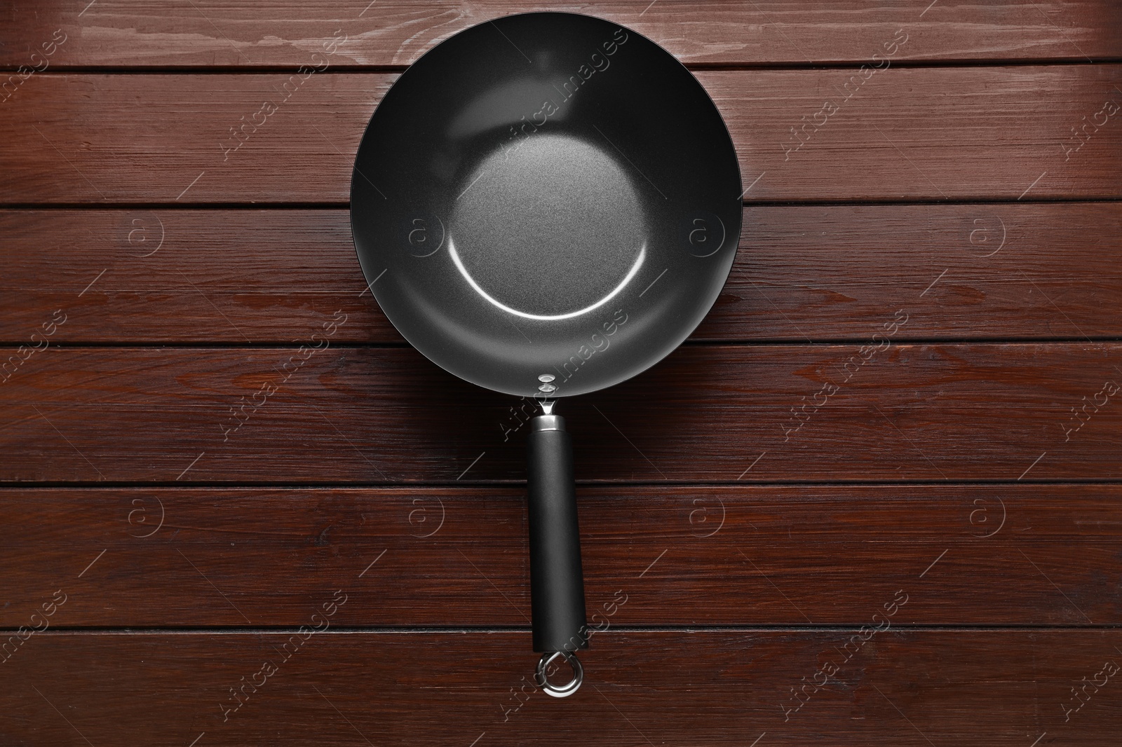 Photo of Empty iron wok on dark wooden table, top view. Chinese cookware