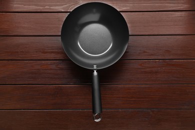 Photo of Empty iron wok on dark wooden table, top view. Chinese cookware