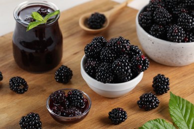 Photo of Tasty blackberry jam and fresh berries on wooden board, closeup
